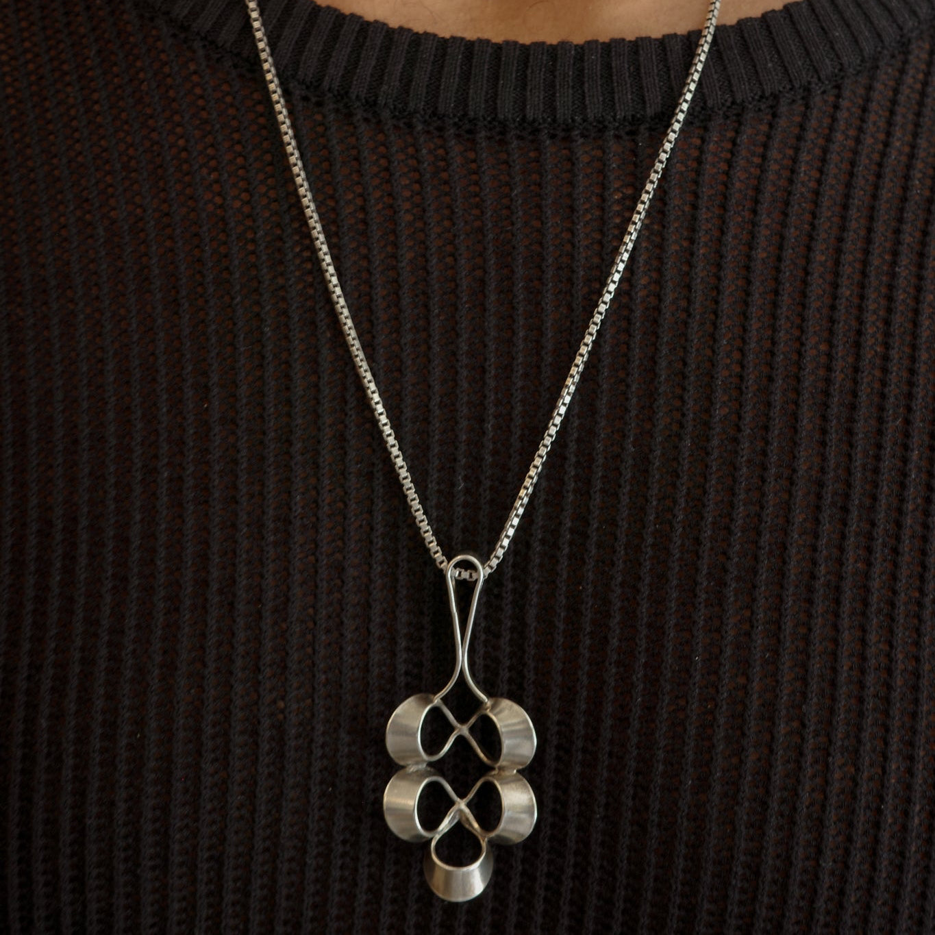 Silver necklace with a pendant worn by a person against a neutral background
