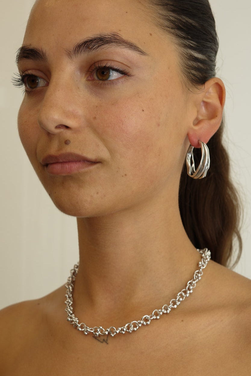 Woman wearing a silver necklace and hoop earrings against a plain background
